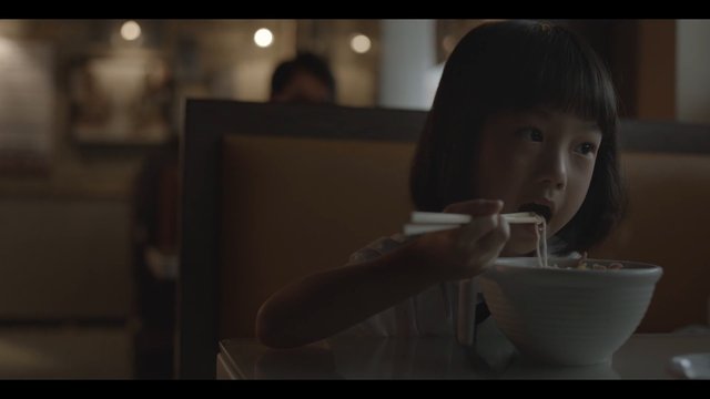 Video Reference: child, restaurant, noodles, chopsticks, bowl, eating, booth, dining, indoors, low light, meal, asian cuisine