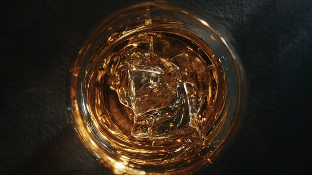 Video Reference: drink, glass, ice, amber, beverage, cocktail, whiskey, alcohol, top view, close-up, dark background, liquid, refreshment