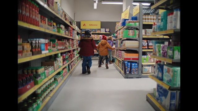 Video Reference: supermarket, grocery store, aisle, shelves, shopping, people, children, winter clothing, candy, packaged goods, retail, indoor, store, walking