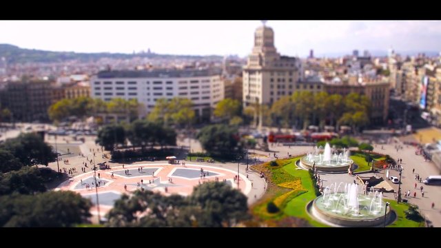 Video Reference: city square, fountain, aerial view, urban plaza, historic buildings, park, downtown, architecture, tourists, landscape, panorama, travel, public space, tilt shift