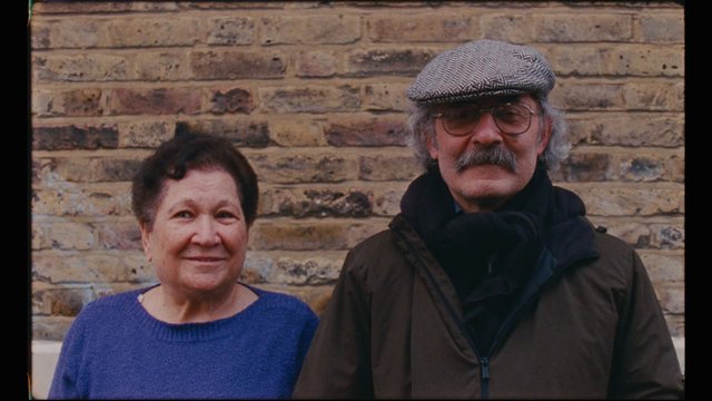 Video Reference: people, portrait, older adults, man, woman, brick wall, outdoor, casual clothing, hat, glasses, mustache, standing, pair, smiling, portrait photography