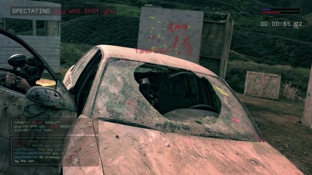 Video Reference: video game, spectator view, car, damaged vehicle, shattered window, paintball, outdoor arena, HUD, chat overlay, first-person, action game, paint splatter, cover, players, timers, match