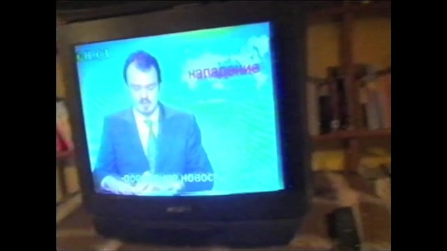 Video Reference: television, CRT, news, broadcast, man, suit, anchor, indoor, screen, retro, blurry, living room, Russian text, monitor