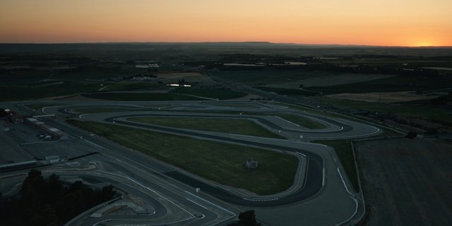 Video Reference: aerial, racetrack, race track, test track, circuit, curves, asphalt, sunset, landscape, rural, empty track, drone view, outdoor, motion course