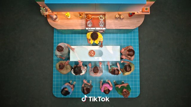 Video Reference: overhead, kitchen, people, group, pizza, table, cooking, studio, colorful, top view, indoor, social gathering, meal, food, counter, apron