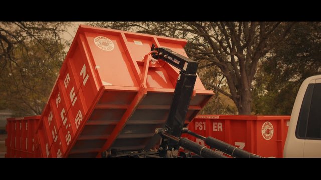 Video Reference: dump trailer, hydraulic arm, truck, red equipment, construction, hauling, outdoor, trees, utility vehicle, metal container, worksite, transport