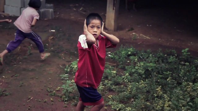 Video Reference: boy, child, outdoors, dirt, running, standing, hands on ears, red shirt, playground, village, rural, play, motion, people