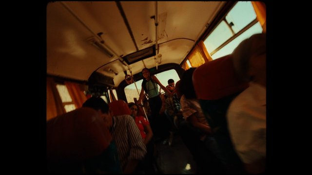 Video Reference: bus interior, passengers, crowded, public transport, standing people, seated people, window light, warm tones, tilted angle, travel, commute, vehicle interior