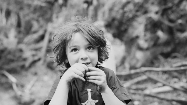 Video Reference: child, portrait, black and white, outdoors, close-up, young, nature, candid, blurred background, face, hands, hair, bokeh, neutral expression