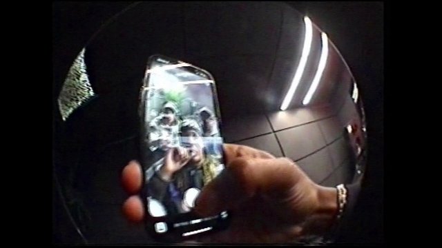 Video Reference: reflection, smartphone, hand, curved surface, indoor, ceiling tiles, dim lighting, close-up, selfie, screen, glossy, metallic, people, fisheye, abstract
