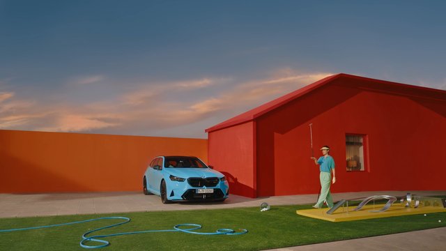 Video Reference: sedan, car, blue car, red house, orange wall, lawn, person, outdoor, sunset, modern design, colorful, residential, driveway, art installation, minimalist, architecture